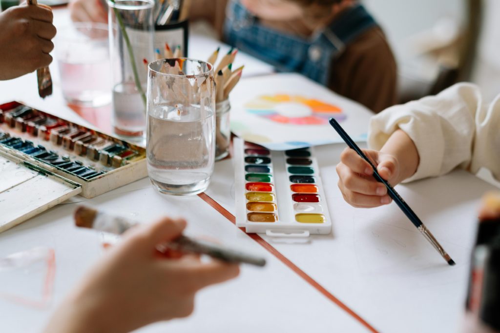 Children's hands holding paintbrushes while painting with watercolors during a creative art session.
